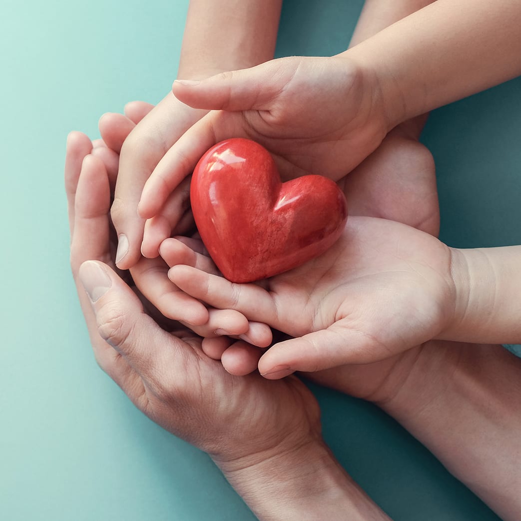 Adult and child hands holding a red heart on an aqua background to signify the importance of heart health, donations, CSR concepts, world heart day, world health day, and family day