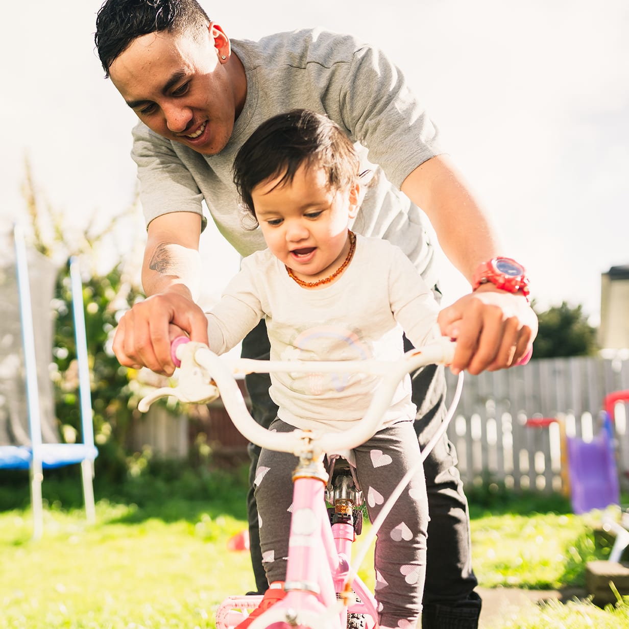 Maori father helping her daughter to ride bicycle in backyard.