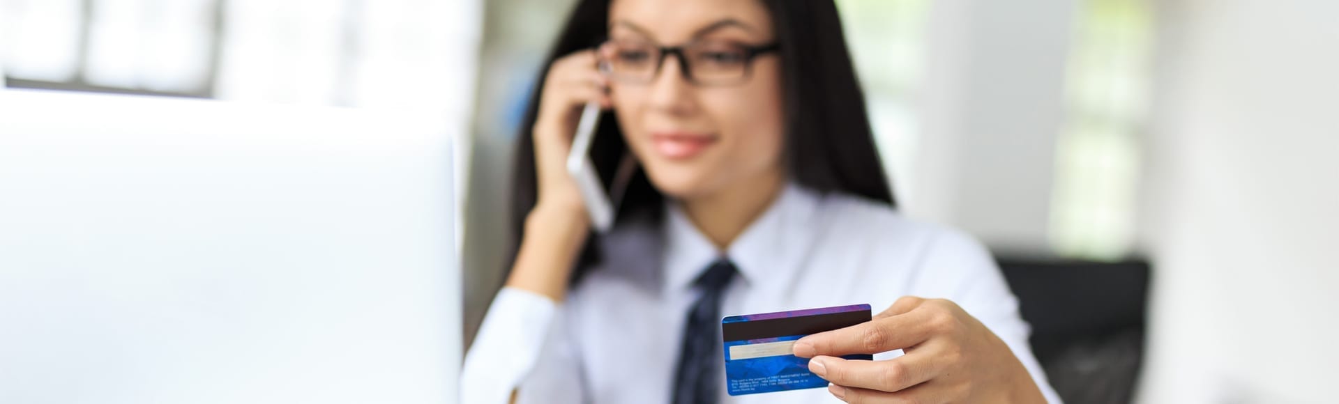 A smiling business woman on the phone holding an aesthetic credit card in hand