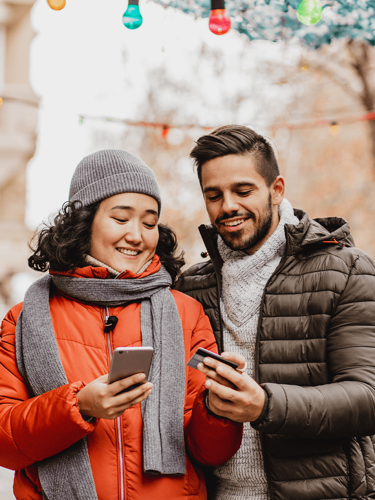 Photo of a man and woman in winter clothing looking at their smart phones