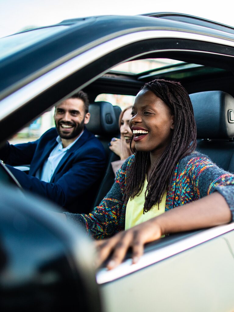 Photo of a woman in the drivers seat of a car and she's smiling. There is a smiling man in the passenger seat